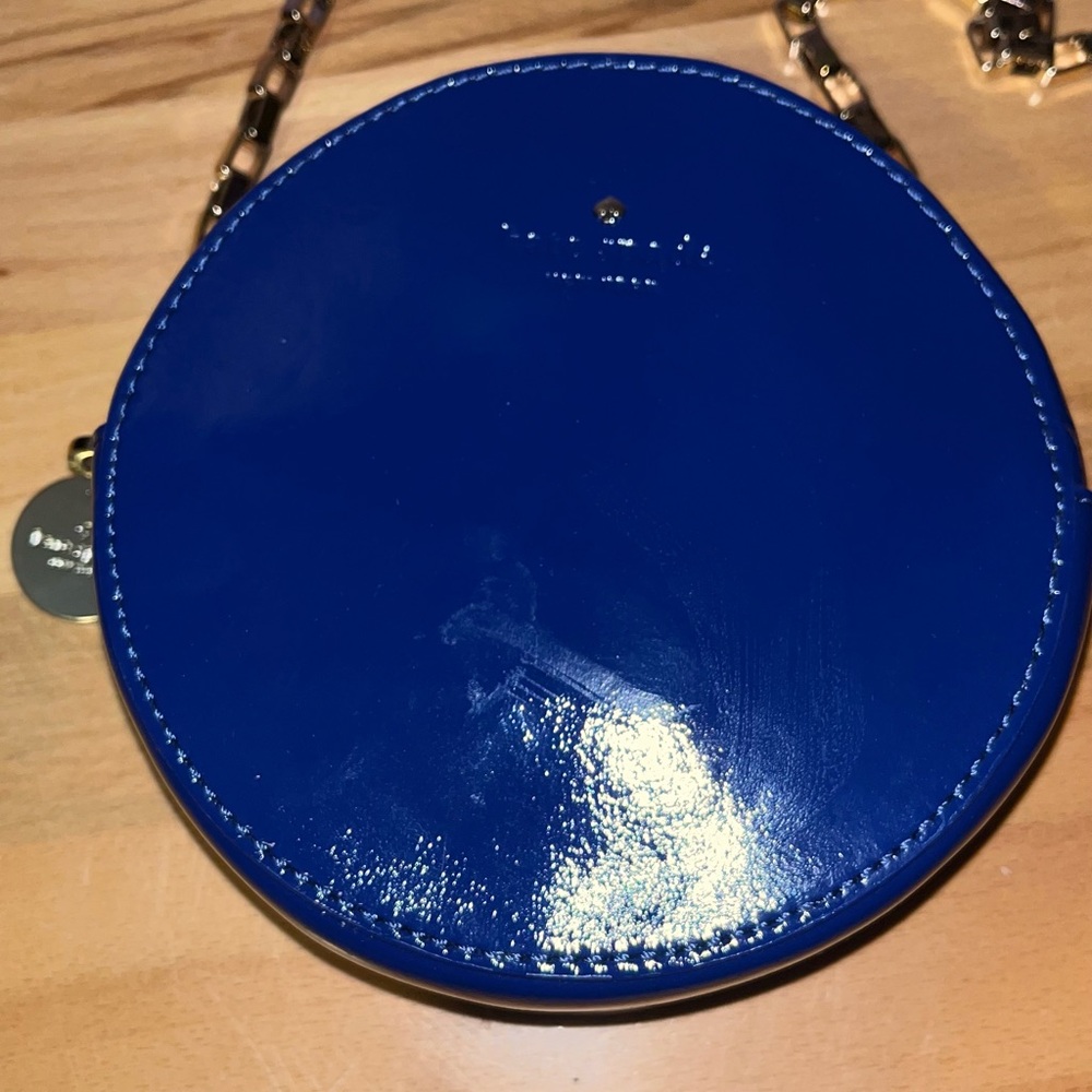 Kate Spade round crossbody bag in blue patent leather with a gold chain strap.
